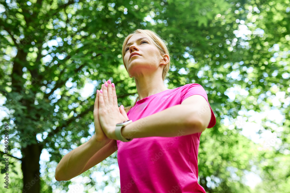 Athletic woman dressed in pink T-shirt and leggings meditates and works out in the park Athletic woman dressed in pink T-shirt and leggings meditates and works out in the park