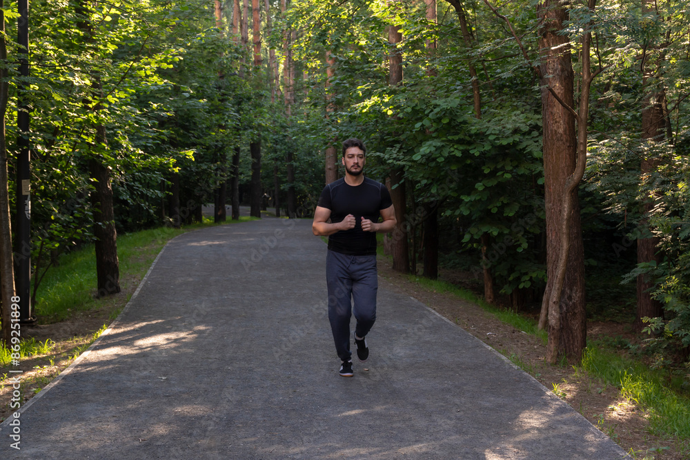 Fototapeta premium Portrait of sporty and handsome man in black sportswear walking in the eco park. Healthy lifestyle and running in open air concept
