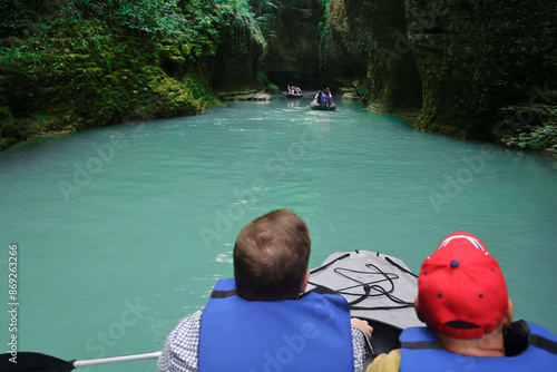 back rear view of Tourists in rubber boats enjoying views of Abasha river erosion canyon in Samegrelo region of  Georgia. Martvili Canyon. male with paddles wear saving vest group  op people floating photo