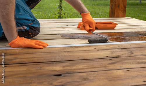 Fotografija Someone in orange gloves stains a wooden deck with a roller