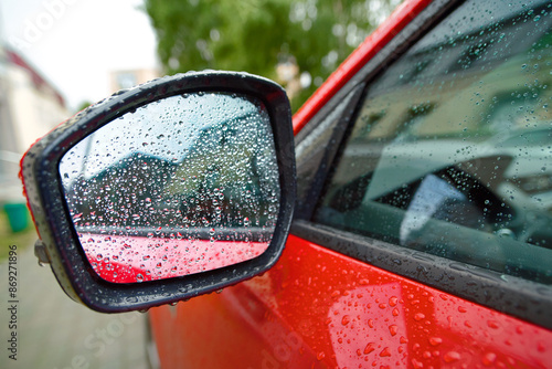 Car mirror and side door covered in rainwater, raindrops and wet exterior during rainy day. Car side mirror and door. Wet car mirror with water drops, non heated side mirror close-up. Selective focus photo