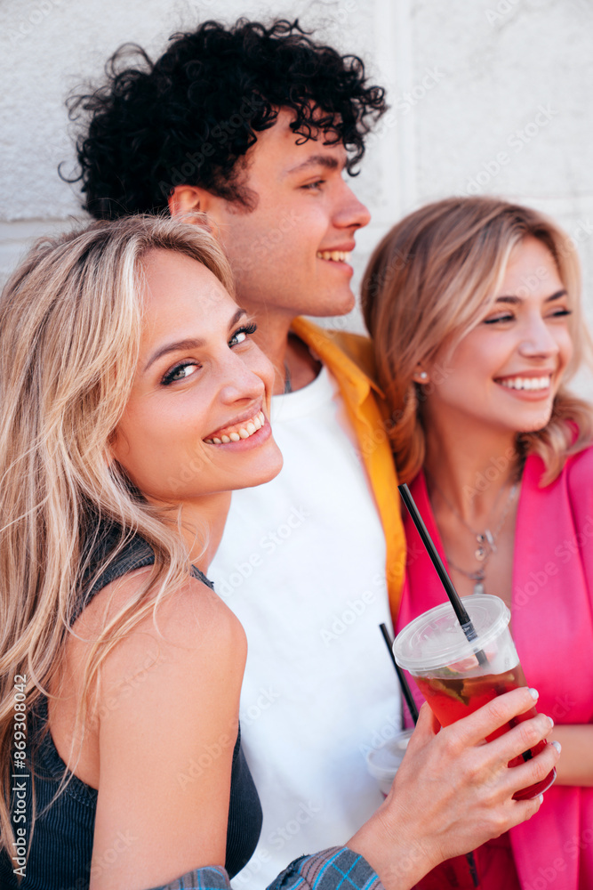 Young three stylish friends posing in the street. Fashion man and two cute female dressed in casual summer clothes. Smiling models having fun. Cheerful women and guy outdoors, Hold and drink lemonade Young three stylish friends posing in the street. Fashion man and two cute female dressed in casual summer clothes. Smiling models having fun. Cheerful women and guy outdoors, Hold and drink lemonade