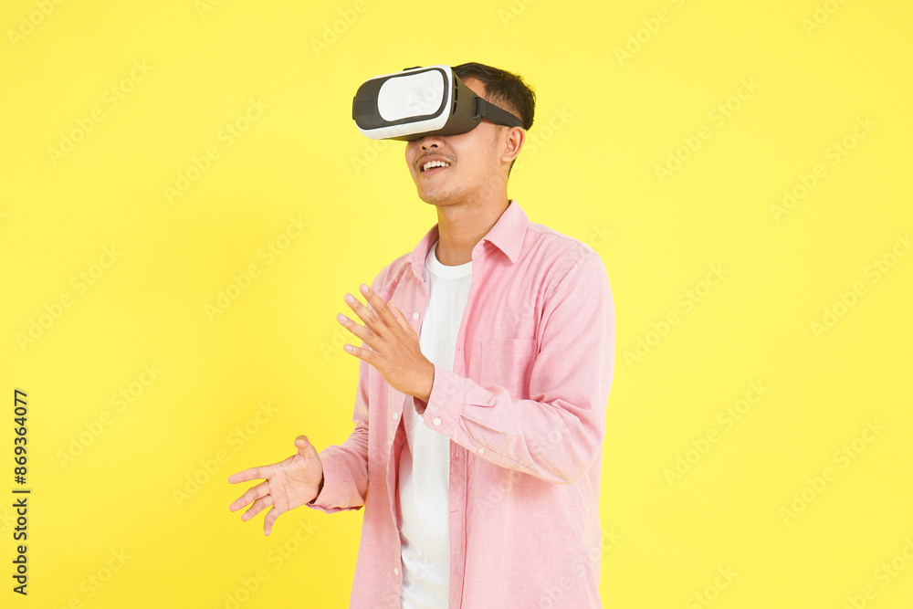Isolated man in pink shirt wearing a VR headset, presentation and interaction with gesturing hands, standing against a light yellow background. Technology, futuristic, modern innovation concepts Isolated man in pink shirt wearing a VR headset, presentation and interaction with gesturing hands, standing against a light yellow background. Technology, futuristic, modern innovation concepts