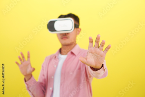 Selective focus on hand of man wearing VR headset and pink shirt, click hand gesture, interacting with a virtual environment on a yellow background