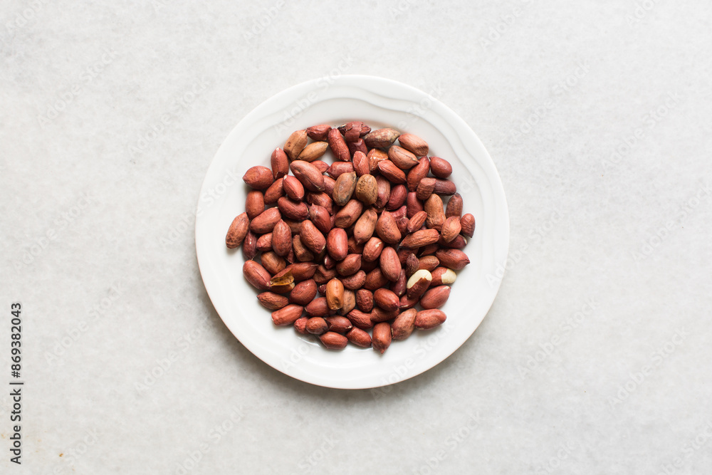 Overhead view of unpeeled raw peanuts on a white plate, flatlay of raw peanuts on a marble countertop, process of making roasted peanuts Overhead view of unpeeled raw peanuts on a white plate, flatlay of raw peanuts on a marble countertop, process of making roasted peanuts
