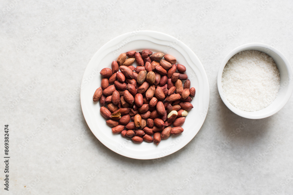 Overhead view of unpeeled raw peanuts and sugar on a marble countertop, flatlay of mise en place of ingredients for making candied peanuts, process of making candied peanuts Overhead view of unpeeled raw peanuts and sugar on a marble countertop, flatlay of mise en place of ingredients for making candied peanuts, process of making candied peanuts