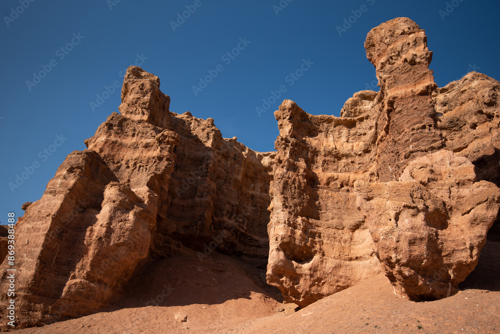 Fototapeta premium Imposing red sandstone cliffs with intricate erosion patterns against a stark blue sky in a desert environment.