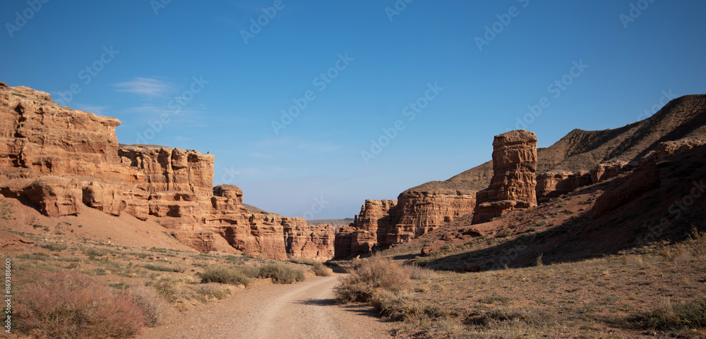 Scenic view of weathered red rock formations along a winding dirt road under a clear blue sky. Scenic view of weathered red rock formations along a winding dirt road under a clear blue sky.