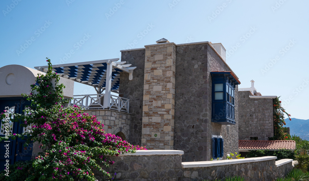 a traditional stone-built house with blue accents and a pergola, amid vibrant bougainvillea, under a clear blue sky, in a Mediterranean coastal region. a traditional stone-built house with blue accents and a pergola, amid vibrant bougainvillea, under a clear blue sky, in a Mediterranean coastal region.
