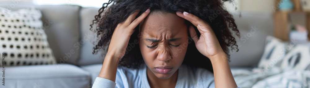 Young African American woman sitting on sofa in pain, holding head with headache. Young African American woman sitting on sofa in pain, holding head with headache.