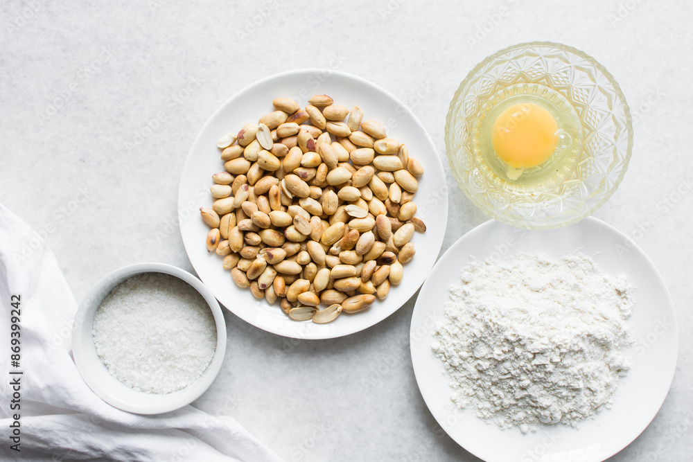 Overhead view of roasted peanuts flour egg and sugar on a marble countertop, flatlay of mise en place of ingredients for making coated peanuts, process of making nigerian coated peanuts  cracker nuts