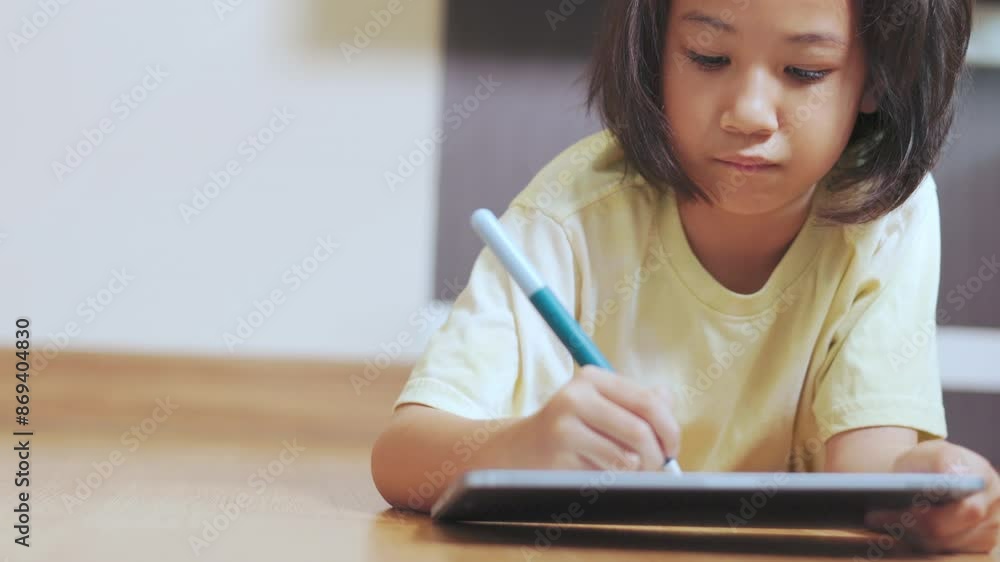 Adorable asian kid girl, drawing or writing on a tablet, lies on the floor of a cozy room. It shows the modern technology and creativity in early education of child for learning and development. Adorable asian kid girl, drawing or writing on a tablet, lies on the floor of a cozy room. It shows the modern technology and creativity in early education of child for learning and development.