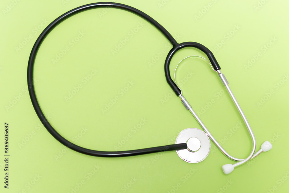 A black and silver stethoscope is on a green background. The stethoscope is a medical instrument used to listen to the sounds of the heart, lungs, and other internal organs A black and silver stethoscope is on a green background. The stethoscope is a medical instrument used to listen to the sounds of the heart, lungs, and other internal organs