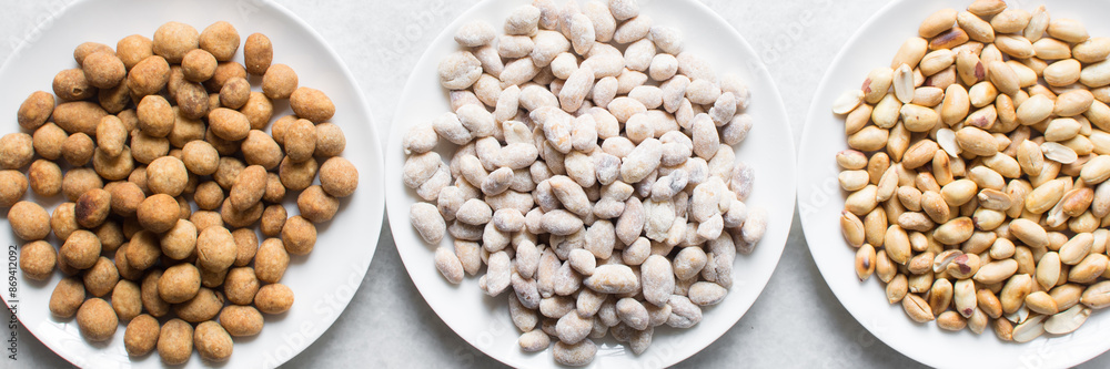 Overhead view of roasted peanuts and coated peanuts on a white plate, flatlay of roasted peeled peanuts and raw coated peanuts on a marble countertop, process of making coated nuts or cracker nuts Overhead view of roasted peanuts and coated peanuts on a white plate, flatlay of roasted peeled peanuts and raw coated peanuts on a marble countertop, process of making coated nuts or cracker nuts