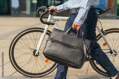 Close-up of a professional carrying a black briefcase, walking a white bicycle, dressed in smart attire.