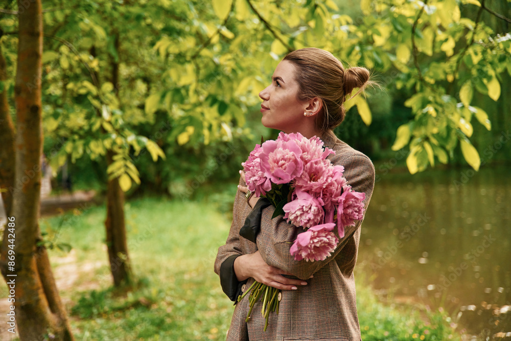 Fototapeta premium Conception of gift of present. Beautiful young woman is with peonies flowers in the park