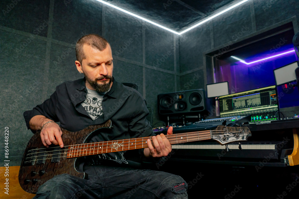 Obraz premium in the equipment of a recording room handsome man with a beard and tattoos plays an electric guitar plucks the strings choosing the right note