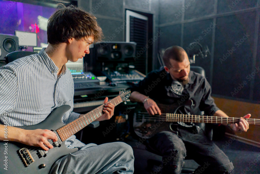 Obraz premium in the equipment of the recording room handsome man with a beard and tattoos and his young friend play the guitar in pairs and act out a song