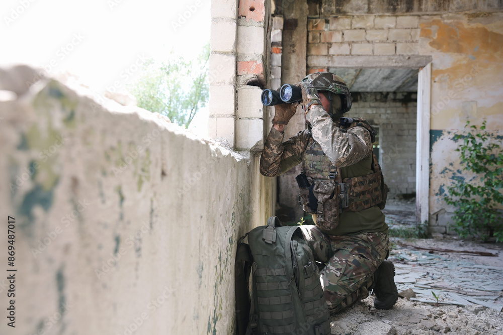 Fototapeta premium Military mission. Soldier in uniform with binoculars inside abandoned building, space for text
