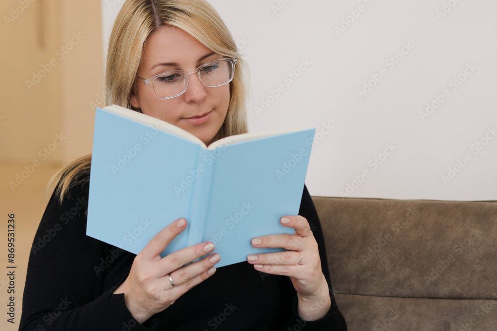 Close up portrait of a caucasian millennial female with glasses siting on a couch and reading a book Close up portrait of a caucasian millennial female with glasses siting on a couch and reading a book