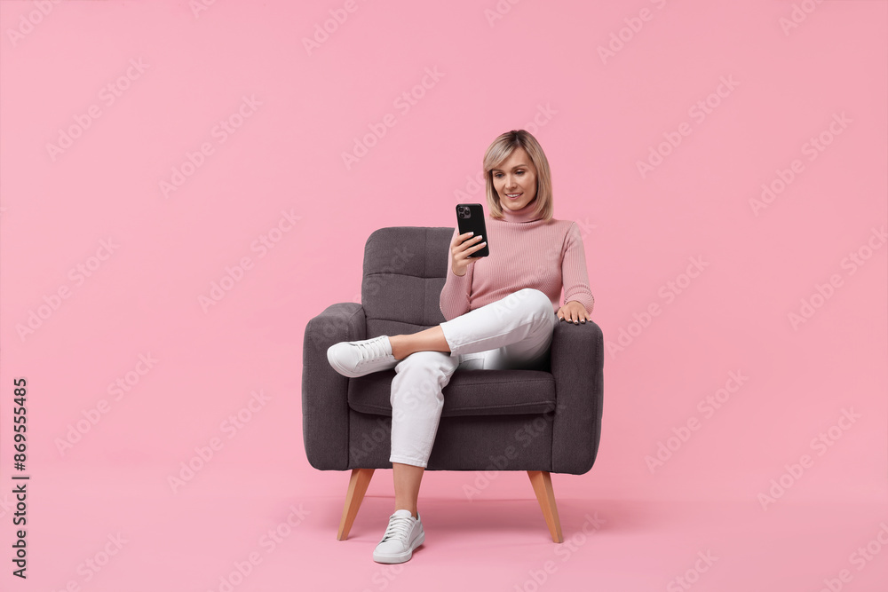 Happy woman with phone on armchair against pink background Happy woman with phone on armchair against pink background
