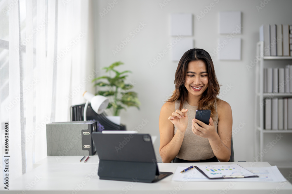 Fototapeta premium A woman is sitting at a desk with a laptop and a cell phone
