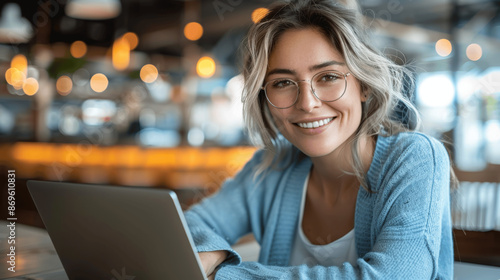 Smiling woman using laptop at a modern cafe table  young professional or student working online  looking at camera