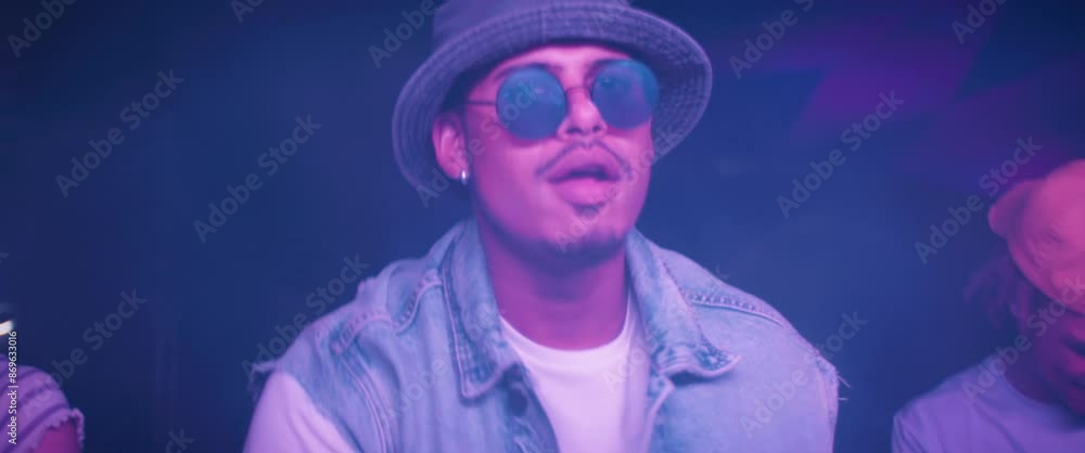 Young man dancing in a crowded festival rave environment wearing sunglasses. Captured using an anamorphic lens and presented in the 2.39:1 CinemaScope aspect ratio. Young man dancing in a crowded festival rave environment wearing sunglasses. Captured using an anamorphic lens and presented in the 2.39:1 CinemaScope aspect ratio.