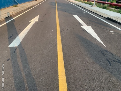 Wallpaper Mural Asphalt Road with White Arrows and Yellow Line. A close-up view of white painted arrows on a grey asphalt road. The arrows indicate direction and guidance for vehicles. Torontodigital.ca