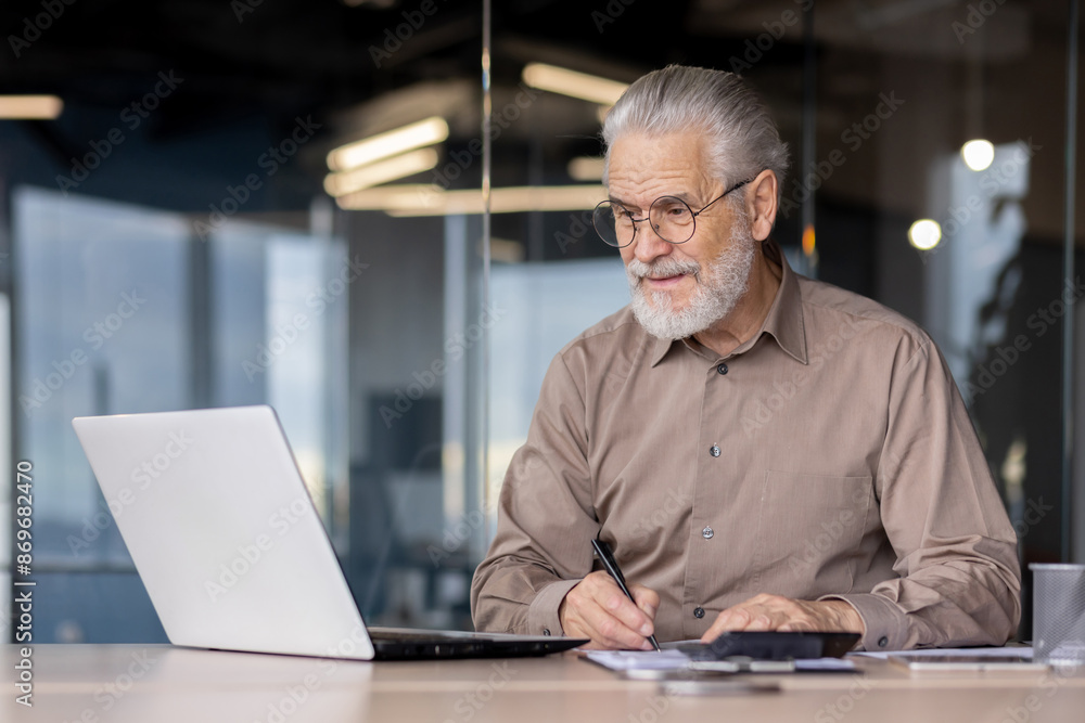 Senior businessman working on a laptop and taking notes in a modern office. The image captures a mature professional in a work environment, showcasing productivity, experience, and dedication Senior businessman working on a laptop and taking notes in a modern office. The image captures a mature professional in a work environment, showcasing productivity, experience, and dedication