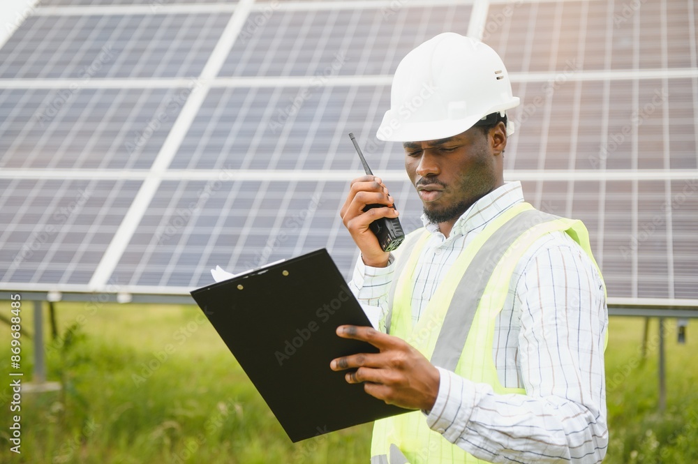 Construction site African worker wearing safety vest and helmet holding a radio, solar panel