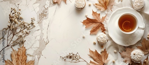 A scene set for fall: a cozy kitchen table with a delicious cup of tea and cake, surrounded by dried maple leaves and beech, against a white countertop with copy space image. © HN Works