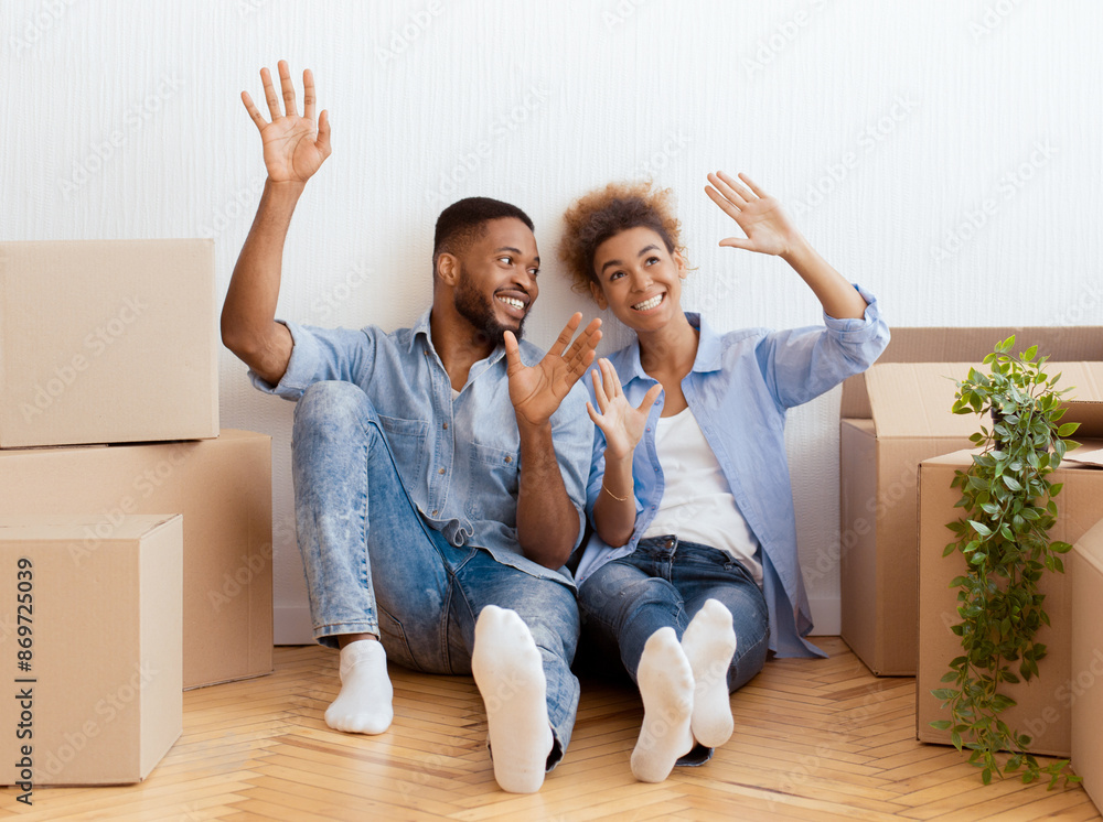 Joyful Black Couple Sitting On Floor Among Moving Boxes Discussing Interior Design And Planning Renovation In New Flat. Joyful Black Couple Sitting On Floor Among Moving Boxes Discussing Interior Design And Planning Renovation In New Flat.