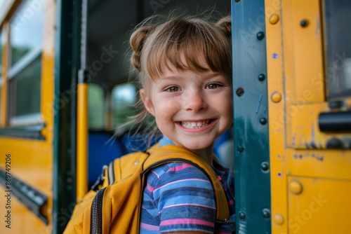 Portrait of a happy little blonde girl with yellow backpack smiling while coming in on doorway of a yellow modern school bus