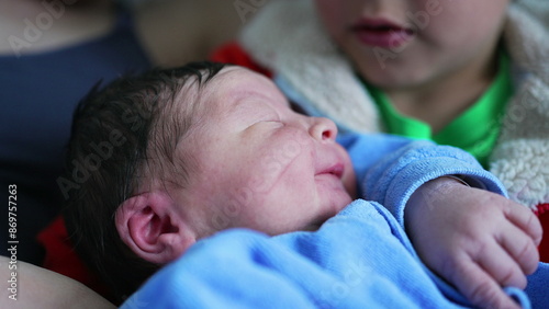 Young sibling gazes adoringly at newborn baby while sitting next to their mother, showcasing a touching moment of sibling bonding and the early development of a loving relationship photo