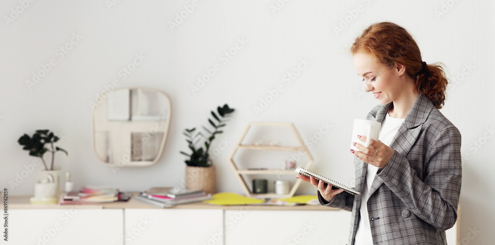 A woman with red hair stands in an office setting, reading notes while holding a cup of coffee. A woman with red hair stands in an office setting, reading notes while holding a cup of coffee.
