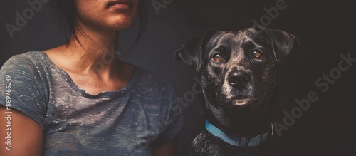 A partial view of a woman standing next to a mixed-breed dog wearing a blue collar, with a black background suitable for copy space image. photo