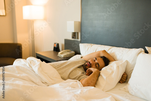 Фотография Caucasian man peacefully sleeps in a cozy hotel room bed, enjoying rest and relaxation