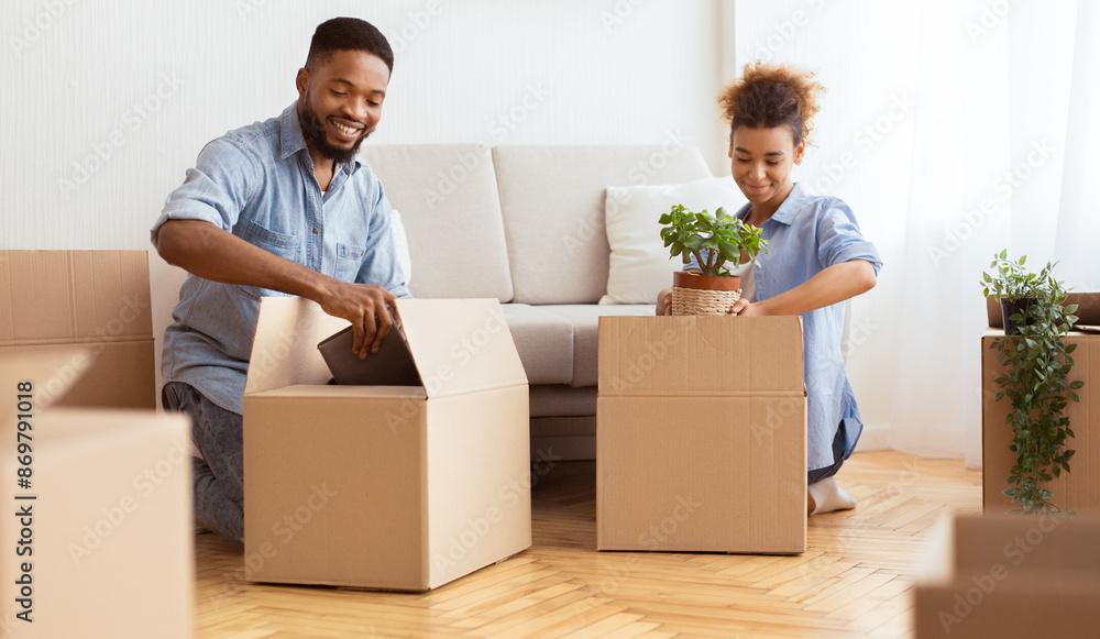 African American Spouses Preparing For Relocation Packing Stuff In Moving Boxes Sitting On Floor Indoor. Selective Focus African American Spouses Preparing For Relocation Packing Stuff In Moving Boxes Sitting On Floor Indoor. Selective Focus