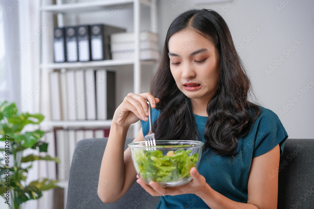 Young woman making disgusted face while eating salad at home Young woman making disgusted face while eating salad at home