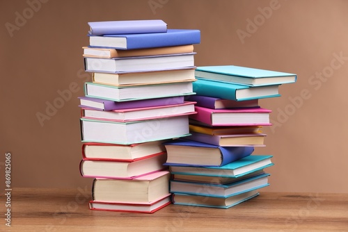 Stacks of colorful books on wooden table against light brown background © New Africa