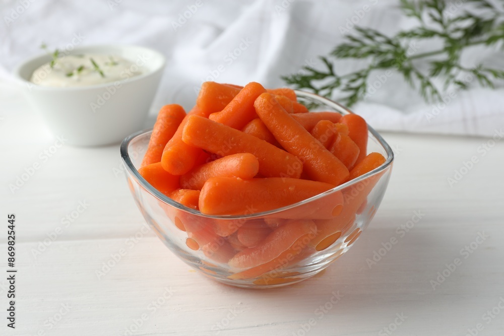 Baby carrots in glass bowl, sauce and green leaf on white wooden table