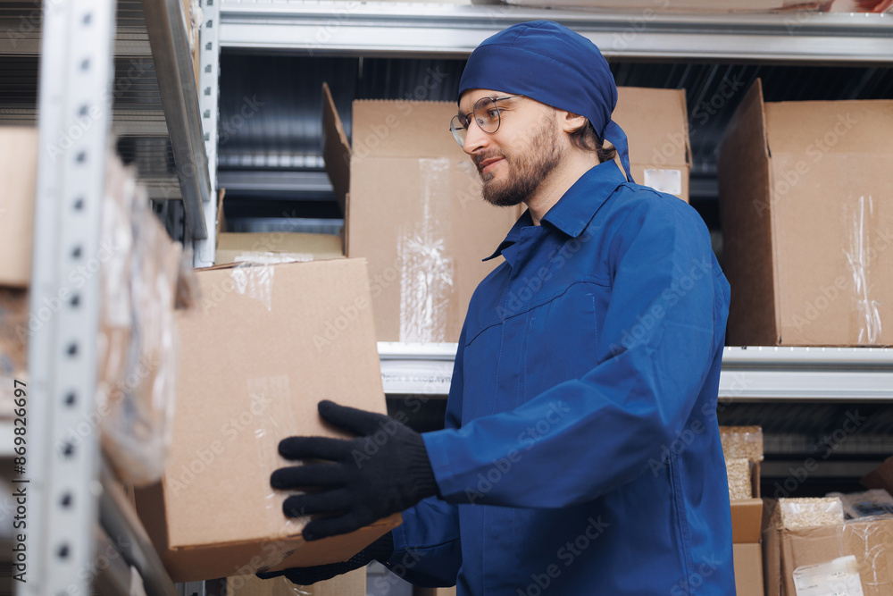 Happy young man loader worker putting a box on a rack in a warehouse Happy young man loader worker putting a box on a rack in a warehouse