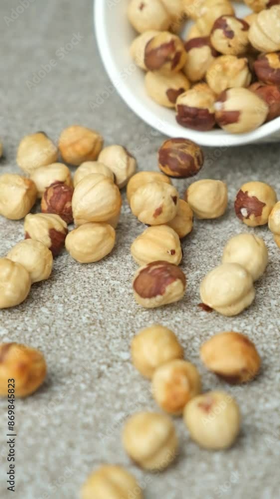 Scattering of peeled hazelnuts on a gray stone background, vertical slow motion Scattering of peeled hazelnuts on a gray stone background, vertical slow motion