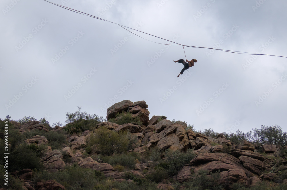 Obraz premium A person is balancing on a tightrope stretched between rocky cliffs.