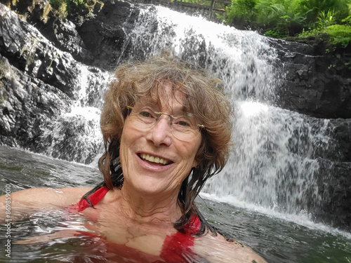 Mature woman wild swimming at Sychryd Falls. Open, wild or cold water swimming is known to have benefits for physical and mental health. She is alone and wearing a red swimming costume. photo