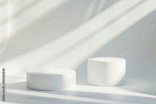 Two white platforms stand against a white backdrop, illuminated by sunlight streaming through a window, creating soft shadows