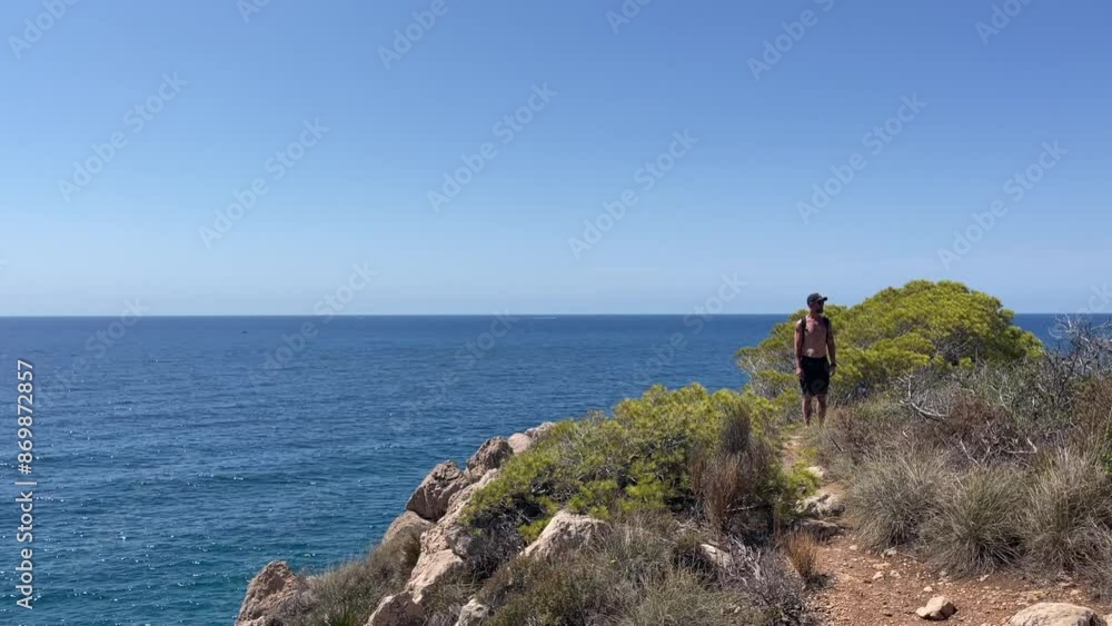 A fit middle-aged man with a backpack stands on a cliff, overlooking the expansive sea. The image captures the essence of adventure, nature, and the tranquility of the ocean A fit middle-aged man with a backpack stands on a cliff, overlooking the expansive sea. The image captures the essence of adventure, nature, and the tranquility of the ocean