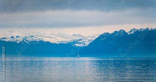Landscape picture of a sailing boat on the Lake Leman, with the and Swiss French Alps on a cloudy and cold day 
