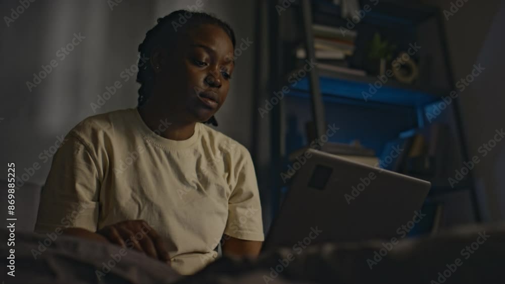 Low angle shot of young African American woman in homewear sitting in unmade bed and ending online session with psychiatrist on laptop, looking tired after sleepless night, having ptsd Low angle shot of young African American woman in homewear sitting in unmade bed and ending online session with psychiatrist on laptop, looking tired after sleepless night, having ptsd